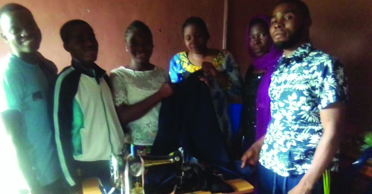 Ahumbe students standing in front of a sowing machine and the clothing they made.