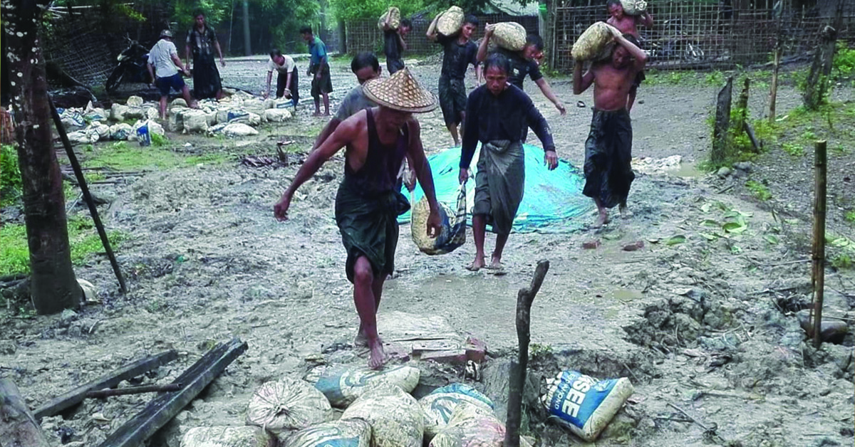 Myanmar villagers putting sandbags on a muddy road.
