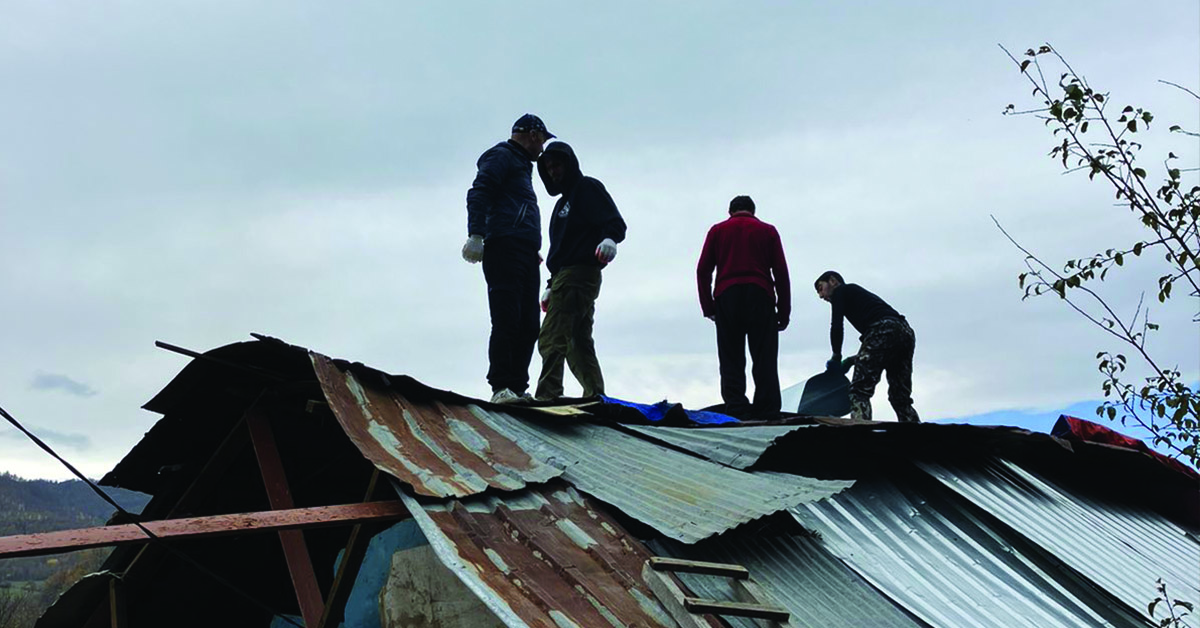 Volunteers and government workers standing on a damaged roof.