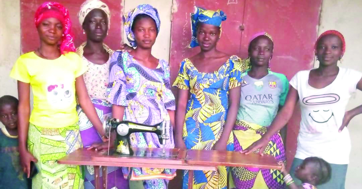 A group of women standing behind a sewing machine.