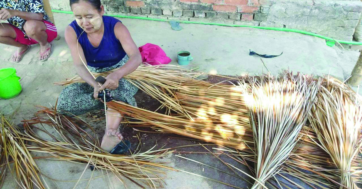 A Myanmar working with large pieces of straw to make a