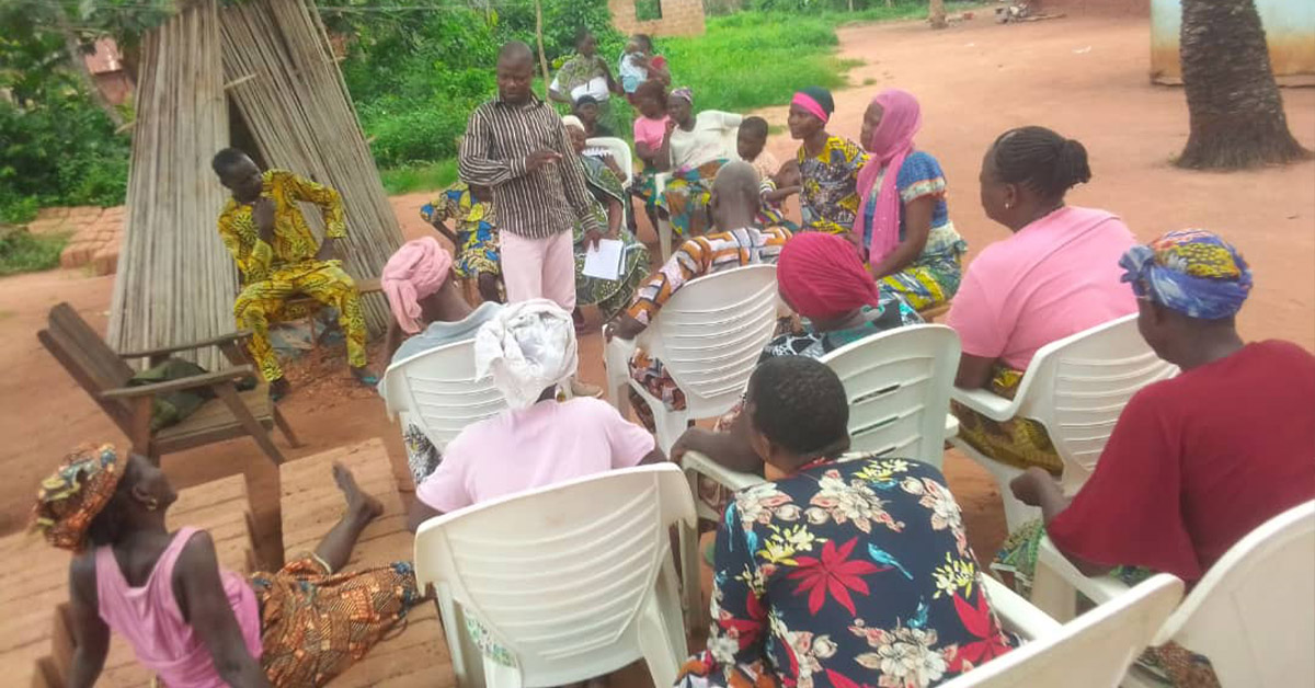 A group of villagers sitting outdoors with chairs while they learn from a TCD worker.