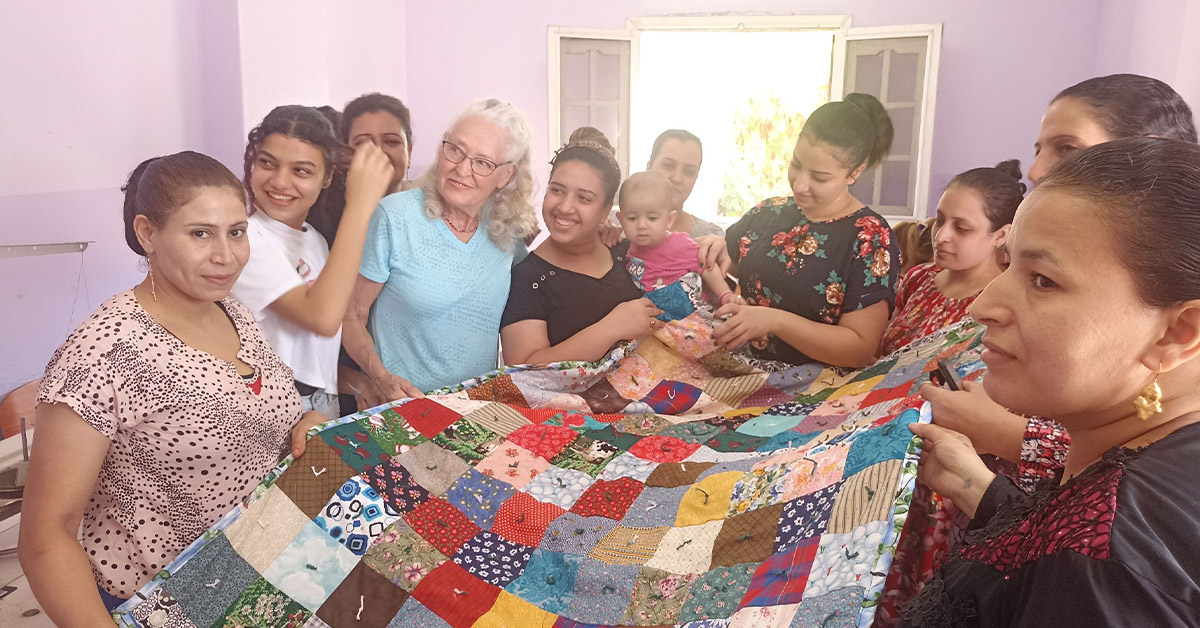 A group of Egyptian women holding a large, quilted blanket together.