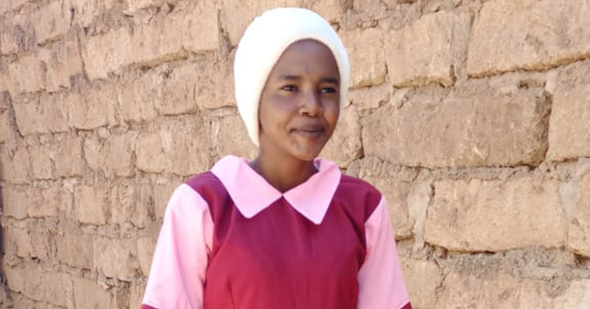 A Kenyan girl in a pink polo and red dress.