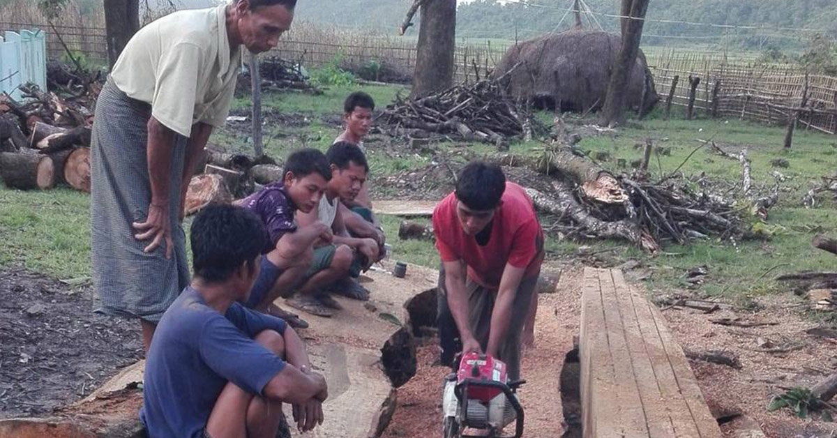 A Myanmar villager using a chainsaw to cut a large piece of wood.