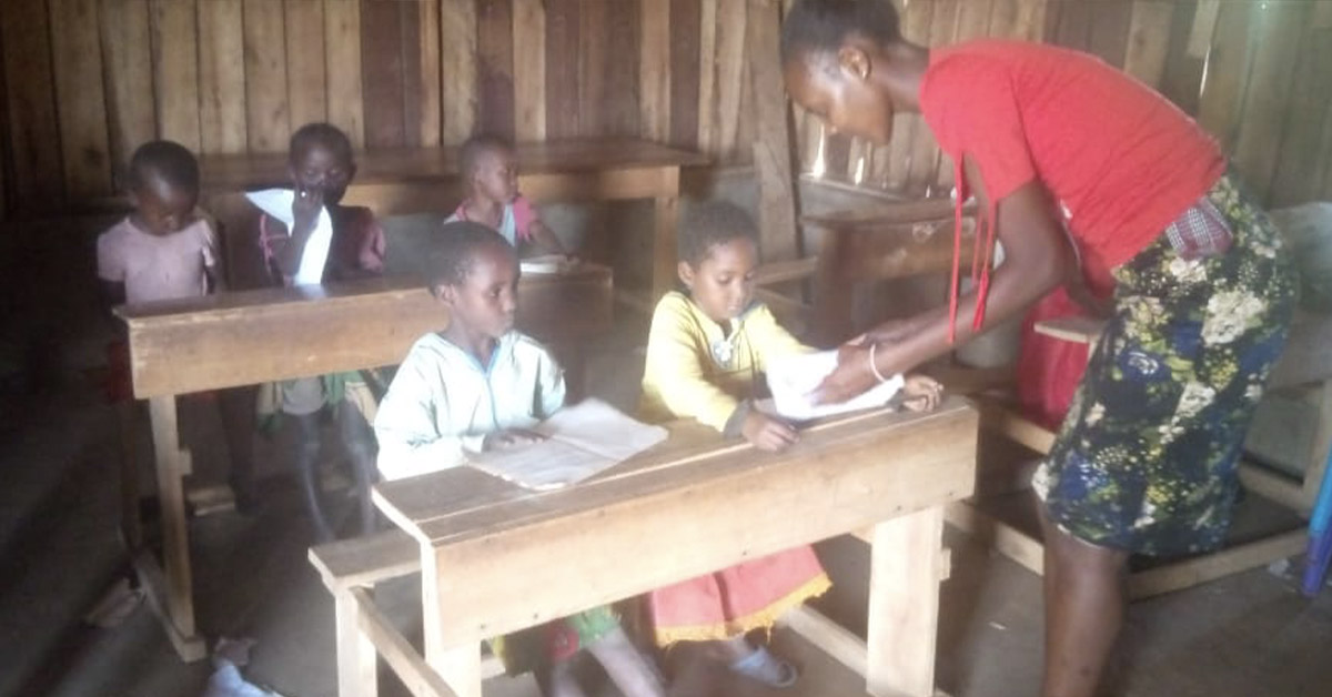 One of the village teachers, Miss Diana, attending the need of one of the students in the classroom.