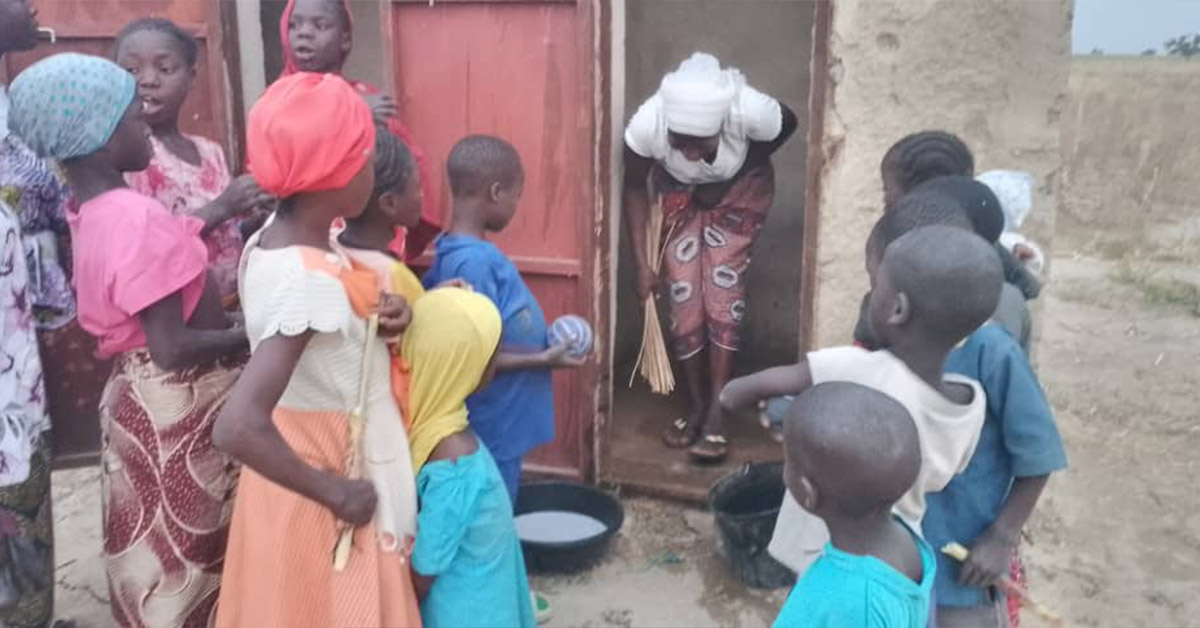 Village children watching an adult villager clean the latrine.