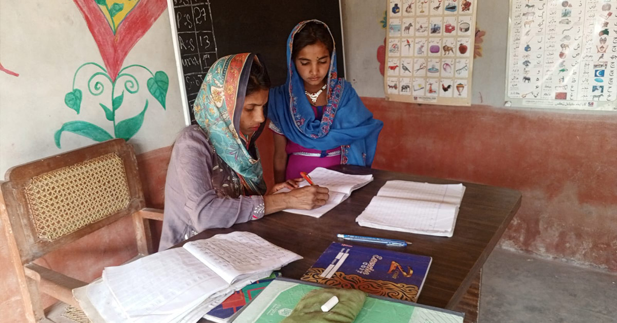 Sindh Province teacher, Saima, writing in a student's notebook.