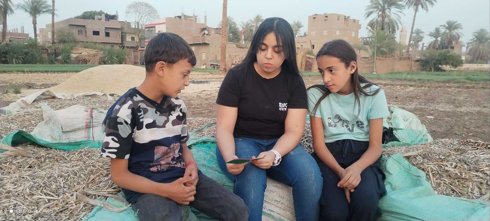 Three Helwan children sitting outdoors and having a discussion.
