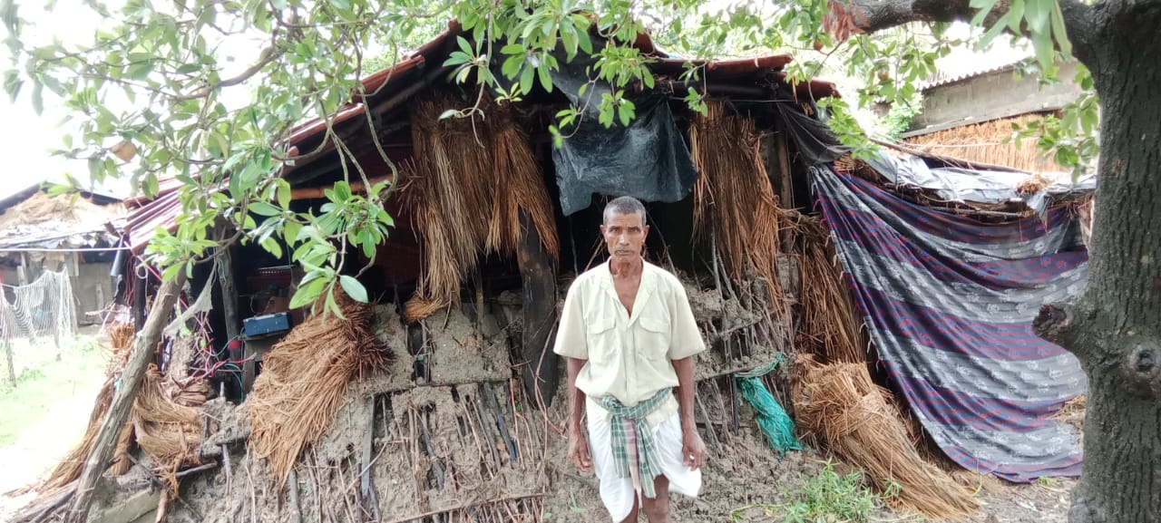 A Binodpur villager standing in front of his large, damaged hut made of straw.