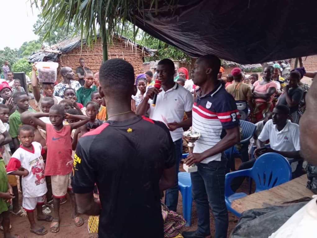 An large crowd of Effaoho villagers listening to the speaker with a microphone.