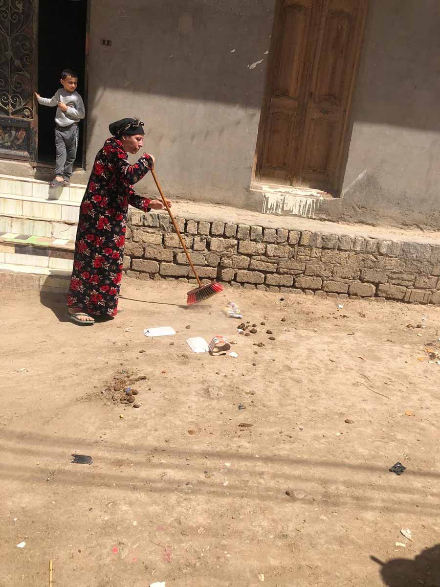 Egyptian villager, Martha, using a large sweeper to brush up the trash around her house.