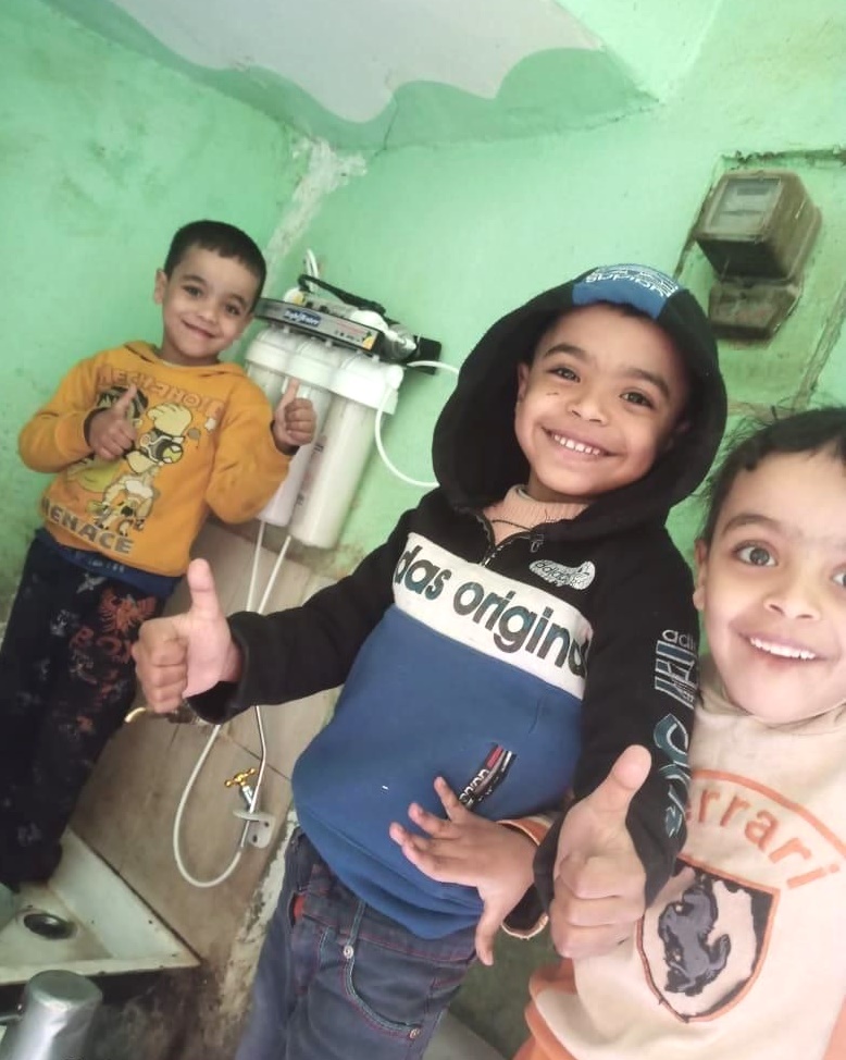Three children giving a thumbs up on the water filter behind them.