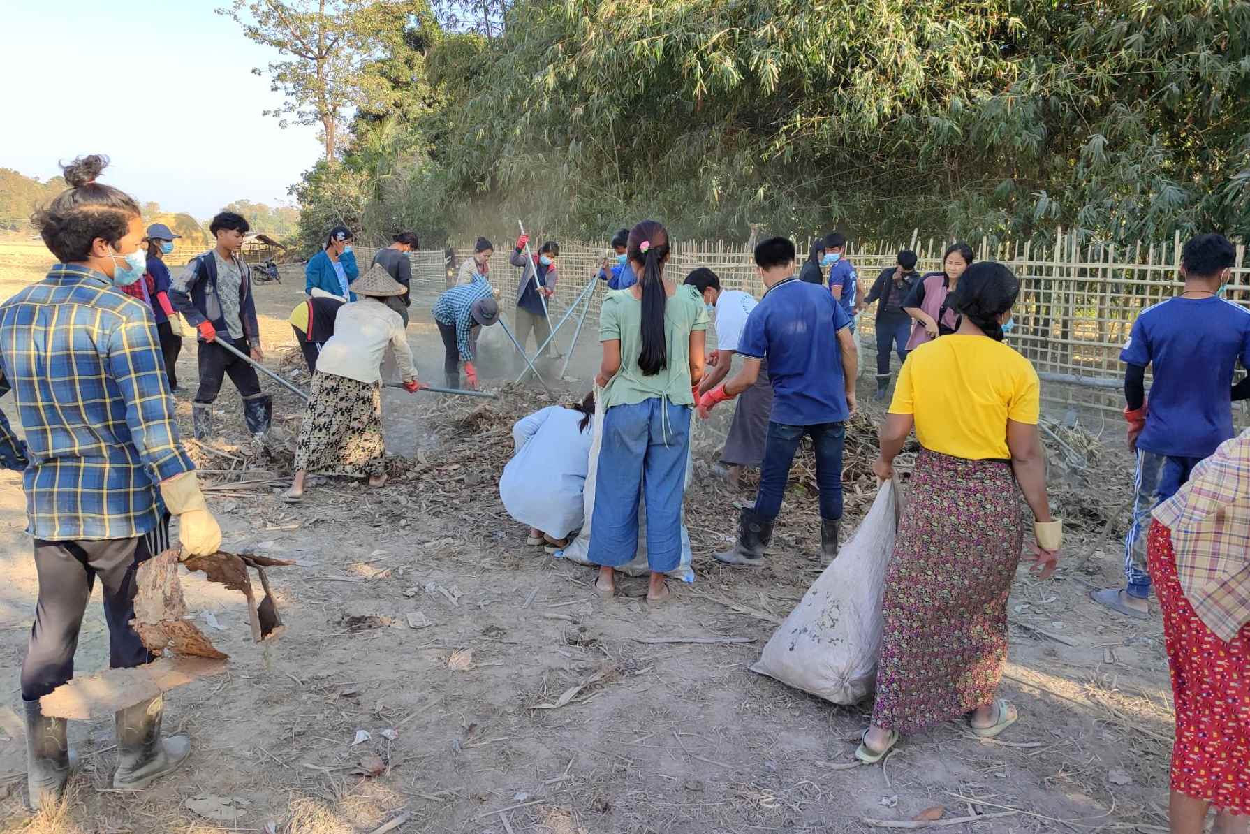 A large group of Myanmar villagers cleaning their community area together.