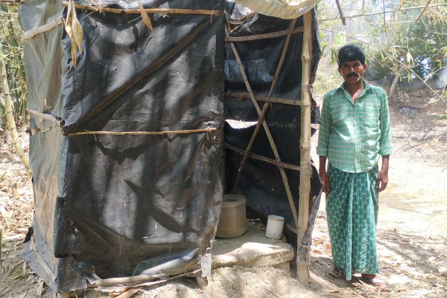 Mr. Mondal from Binodpur village standing in front of his latrine, built with wood and tarp.