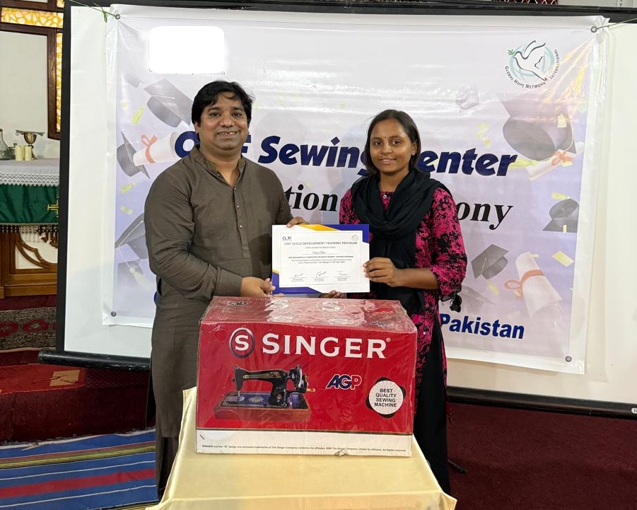 A formal photo of Rahmi with her teacher, sewing machine, and certificate.