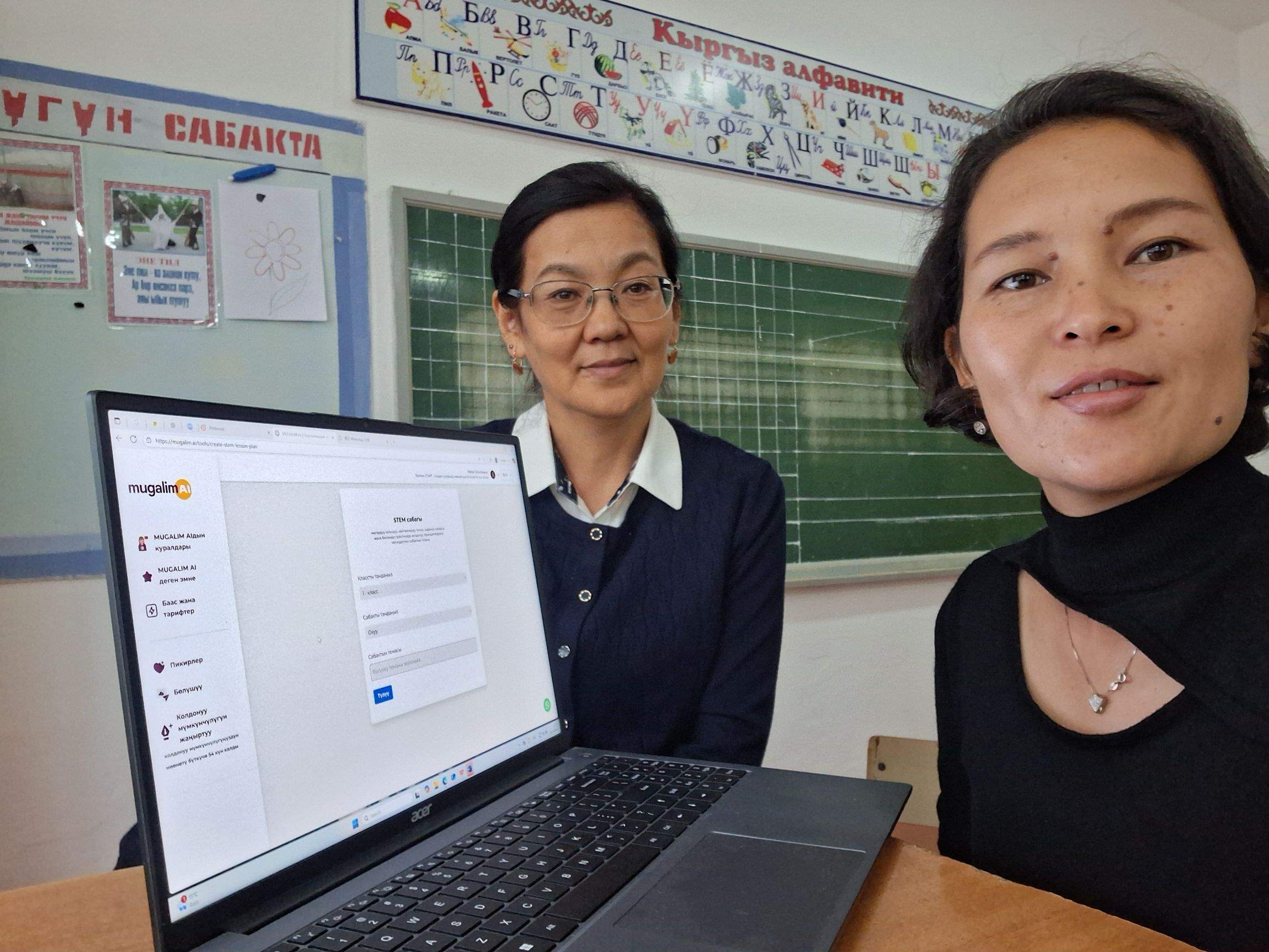 Two women together with a modern laptop in a classroom.