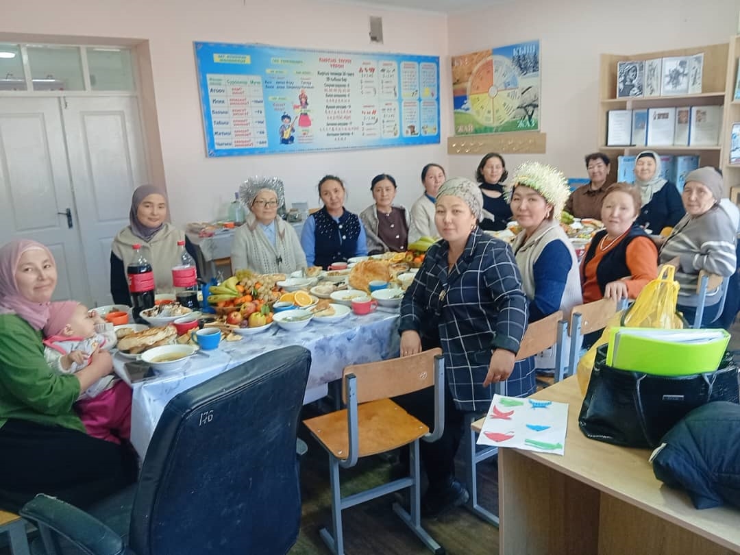 Members of a Kyrgyzstan school posing for a photo with a spread of food for lunch.