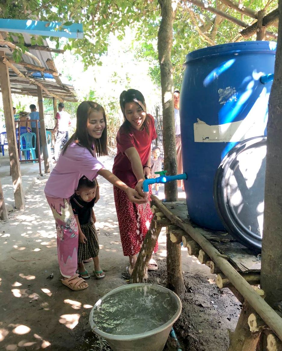 Two Myanmar ladies cupping some water with their hands from the filtration system.