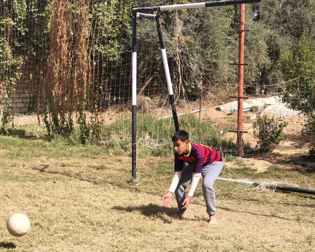 Al Koom Al Ahmar child, Mazen, standing ready to catch the soccer ball as a goalkeeper.